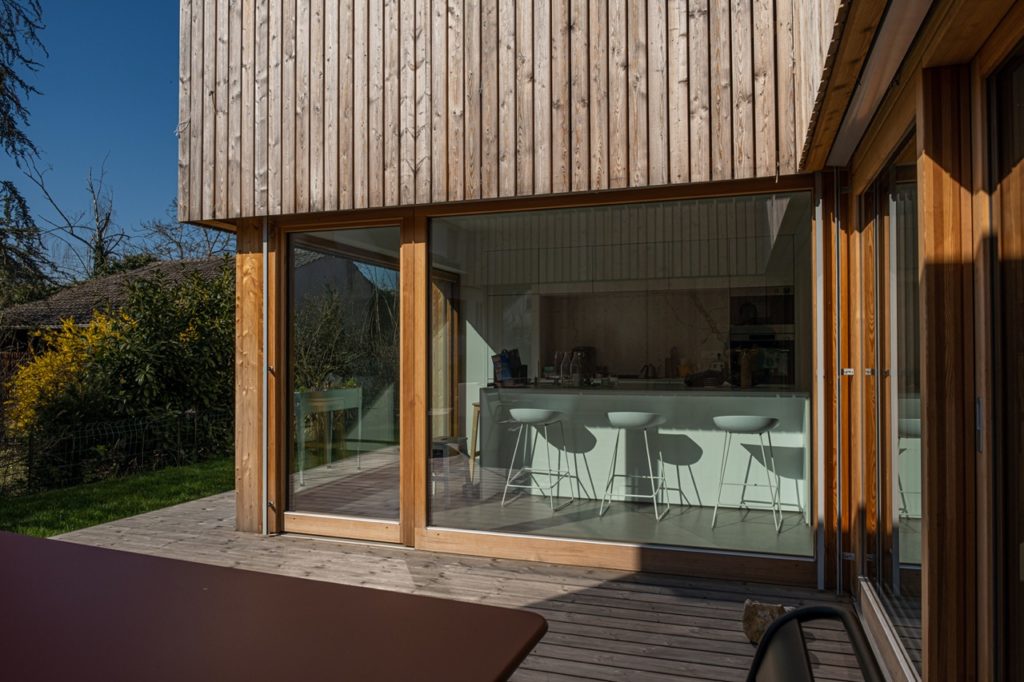 Vue extérieure d'une maison en bois avec baie vitrée donnant sur une salle à manger design 