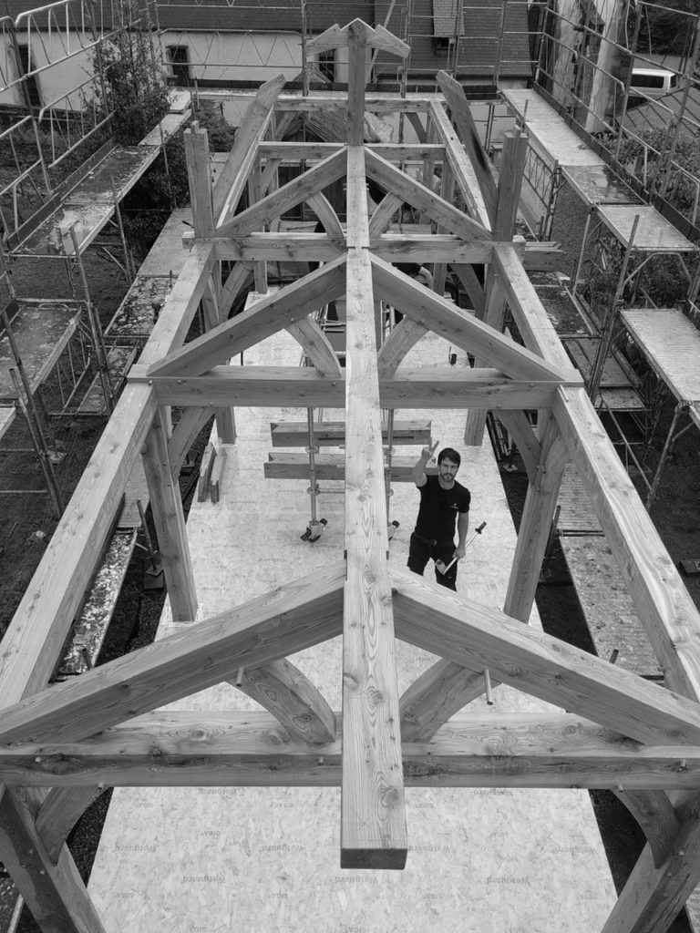 Vue de haut d'une charpente en cours de réalisation avec en contrebas un des artisans de l'Atelier Lignum