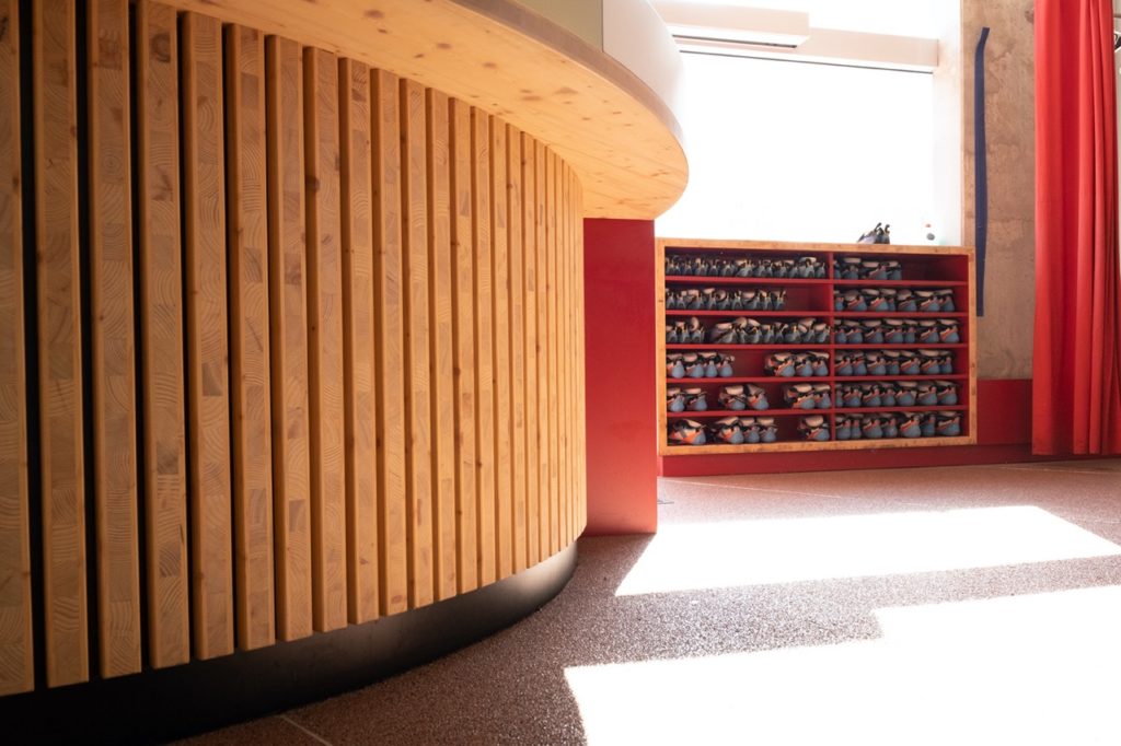 Détail du comptoir d'accueil et d'un meuble de rangement en bois pour chaussons d'escalade