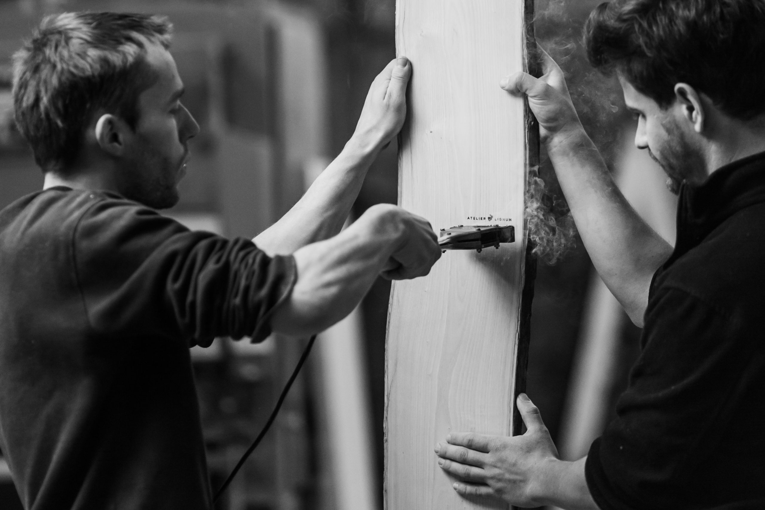 Niels Krüger marquant au fer chaud le logo de l'Atelier Lignum sur une planche en bois tenue par Joseph Barotte.